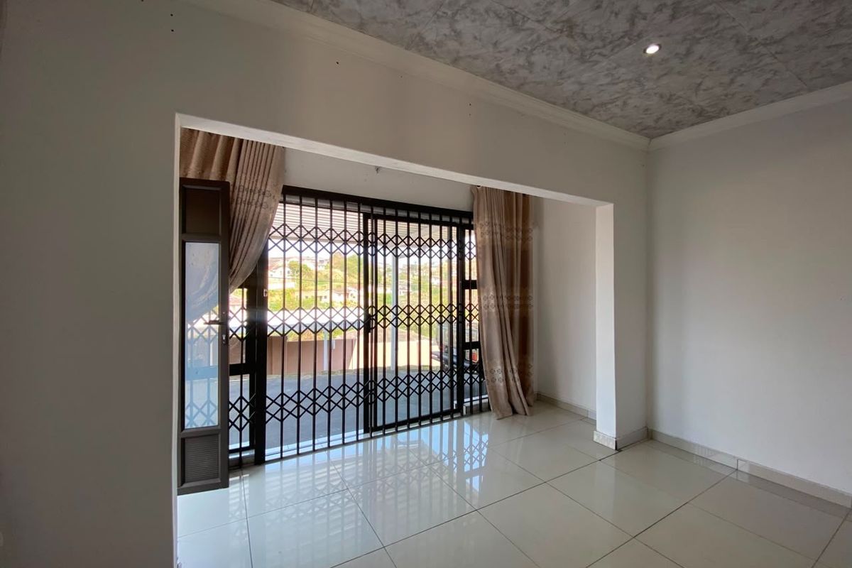 An empty living room featuring tiled flooring, recessed lighting, and a sliding glass door with a security gate leading to the exterior.