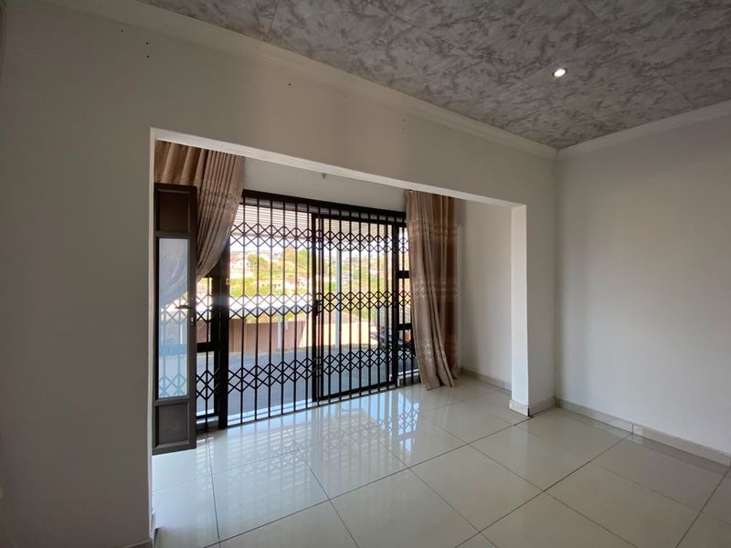 An empty living room featuring tiled flooring, recessed lighting, and a sliding glass door with a security gate leading to the exterior.