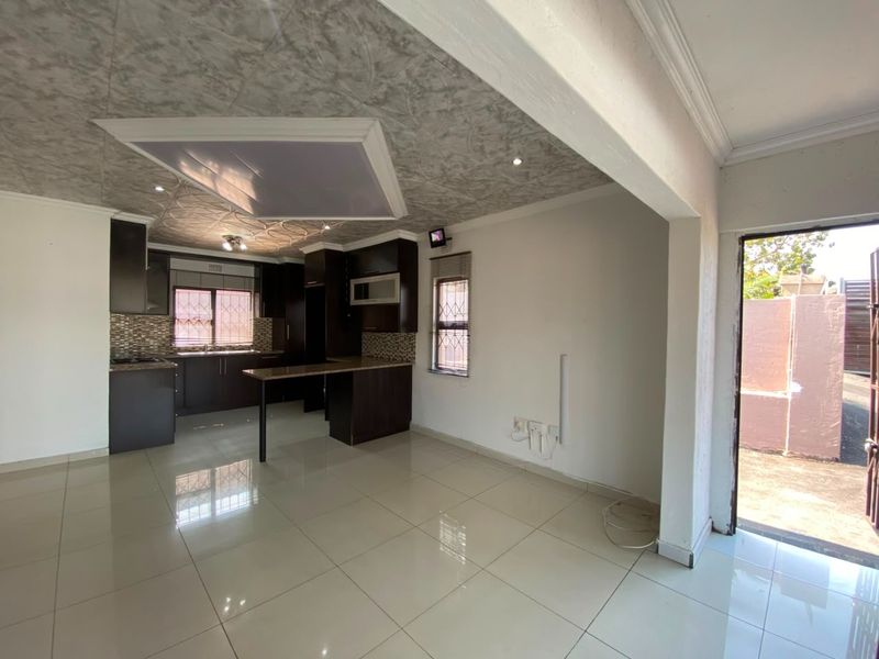 Open-plan kitchen and living area featuring dark cabinetry, granite countertops, tiled flooring, and a breakfast bar, with direct access to the exterior.