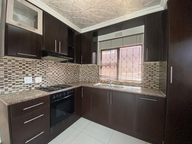 A functional kitchen featuring dark wood cabinetry, granite countertops, a mosaic tile backsplash, and built-in appliances, including an oven and hob.