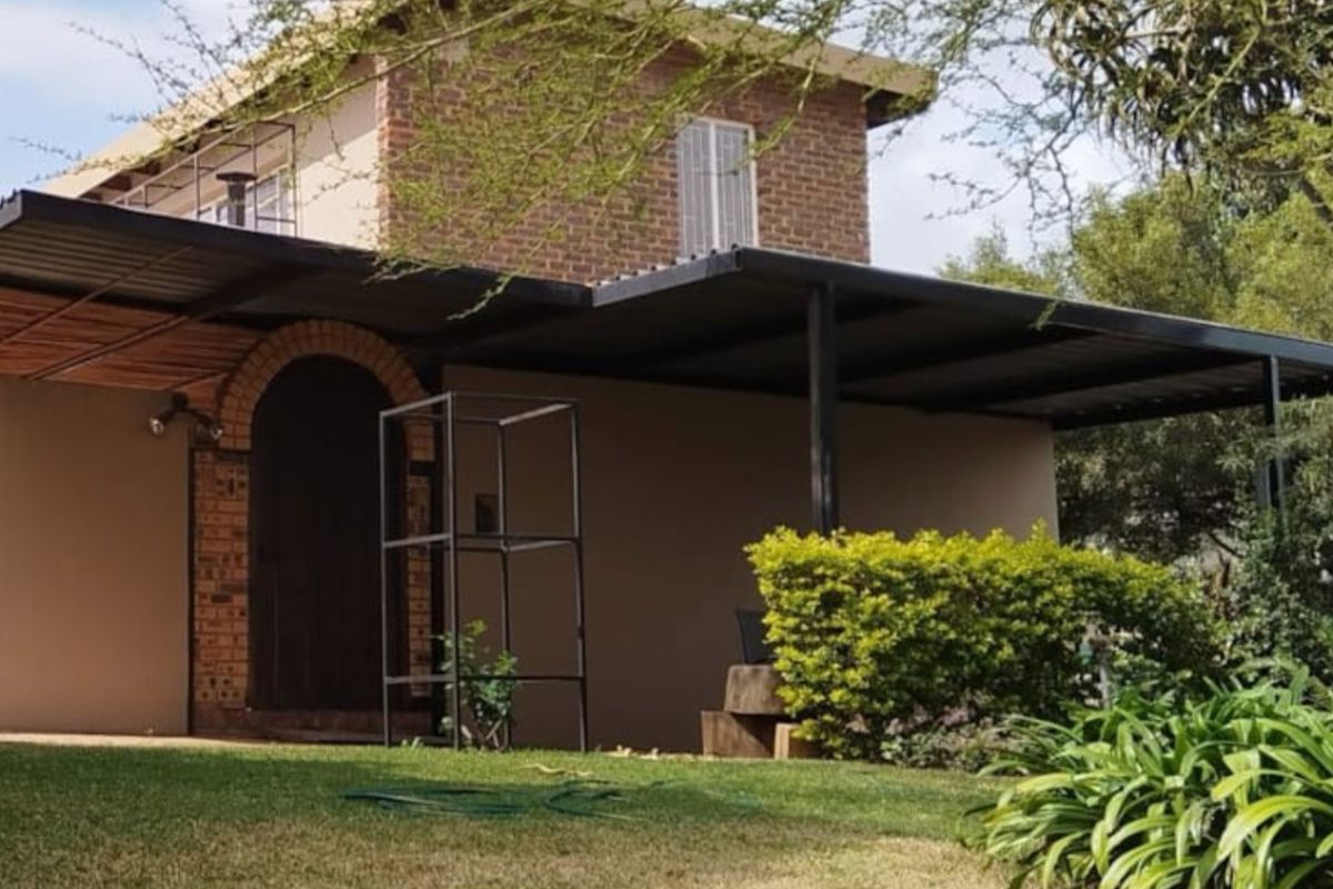 Rear view of a two-story brick house featuring a spacious covered patio area and established garden surroundings.