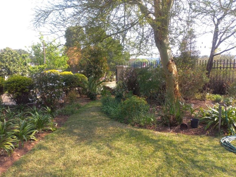 A well-established garden area featuring mature trees, landscaped garden beds, and secure metal perimeter fencing.