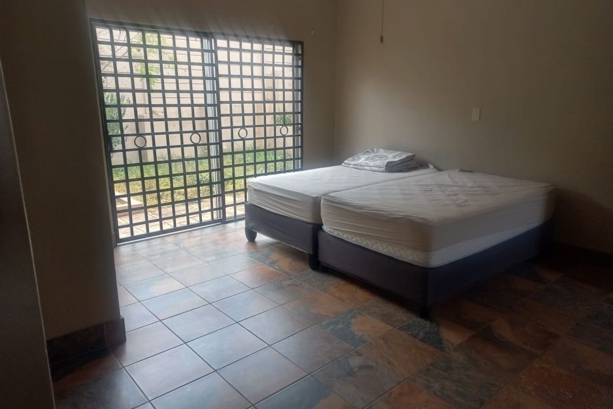 A bedroom featuring tiled flooring, a ceiling fan, and a sliding glass door with an integrated security gate providing access to the exterior.
