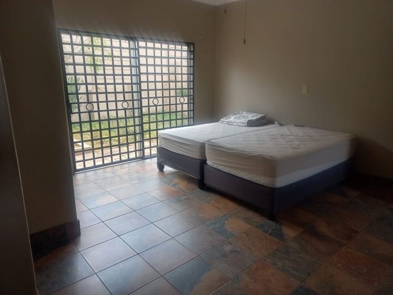 A bedroom featuring tiled flooring, a ceiling fan, and a sliding glass door with an integrated security gate providing access to the exterior.
