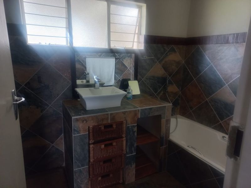 A functional bathroom featuring a tiled vanity with a vessel sink, built-in bathtub, and decorative wall tiling with louvered windows for natural light.