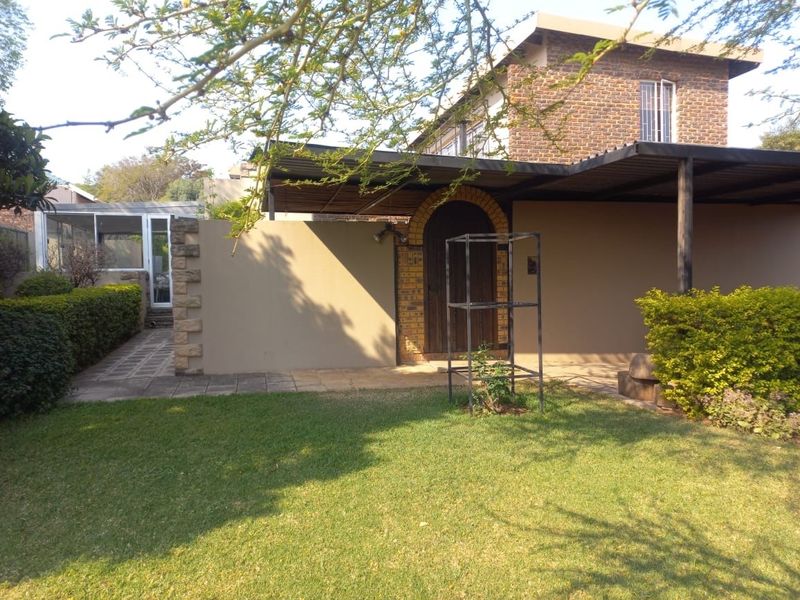 A rear view of the property featuring a brick facade, a covered patio area, and a well-maintained garden with a paved walkway.