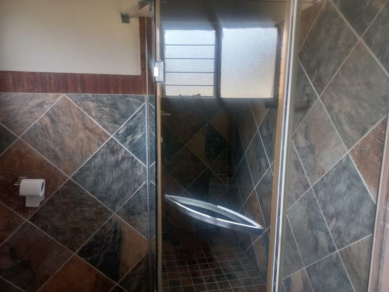 A bathroom featuring a glass-enclosed shower with diamond-patterned wall tiles and an obscured glass window.