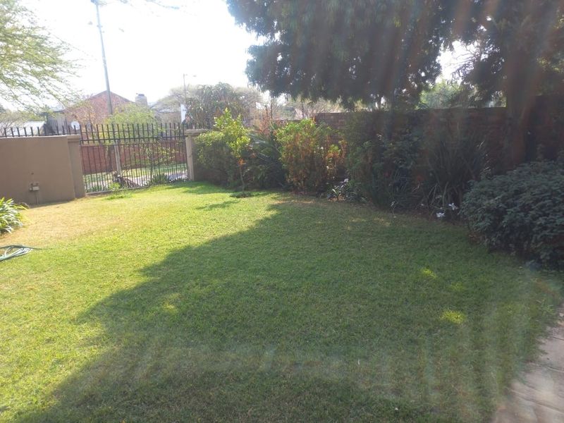 A private rear garden featuring a well-maintained lawn, established perimeter wall, and secure metal fencing.