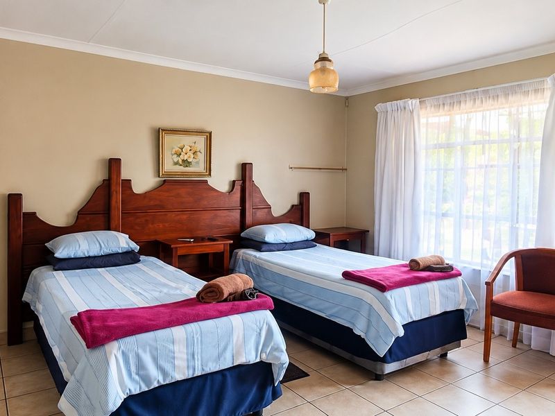 A well-lit bedroom featuring tiled flooring, neutral wall tones, and a large window with curtains, providing a comfortable and functional guest space.