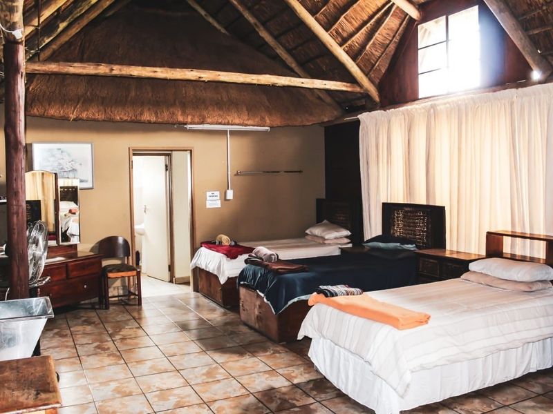 Spacious bedroom featuring a traditional thatched roof with exposed timber rafters, ceramic tiled flooring, and direct access to an en-suite bathroom.