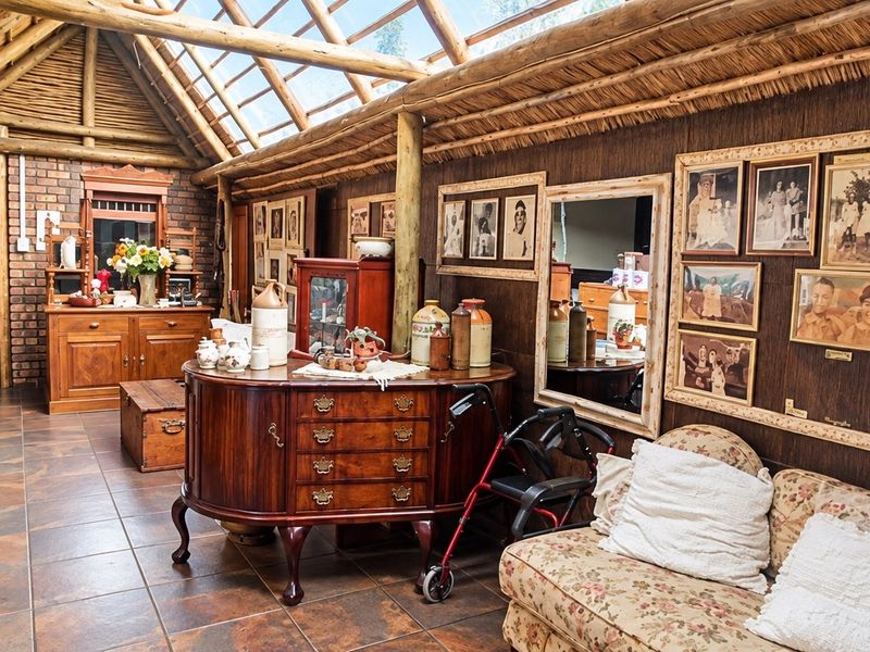 A rustic living area featuring exposed timber rafters, a thatched roof with integrated skylights, exposed brickwork, and durable tiled flooring.