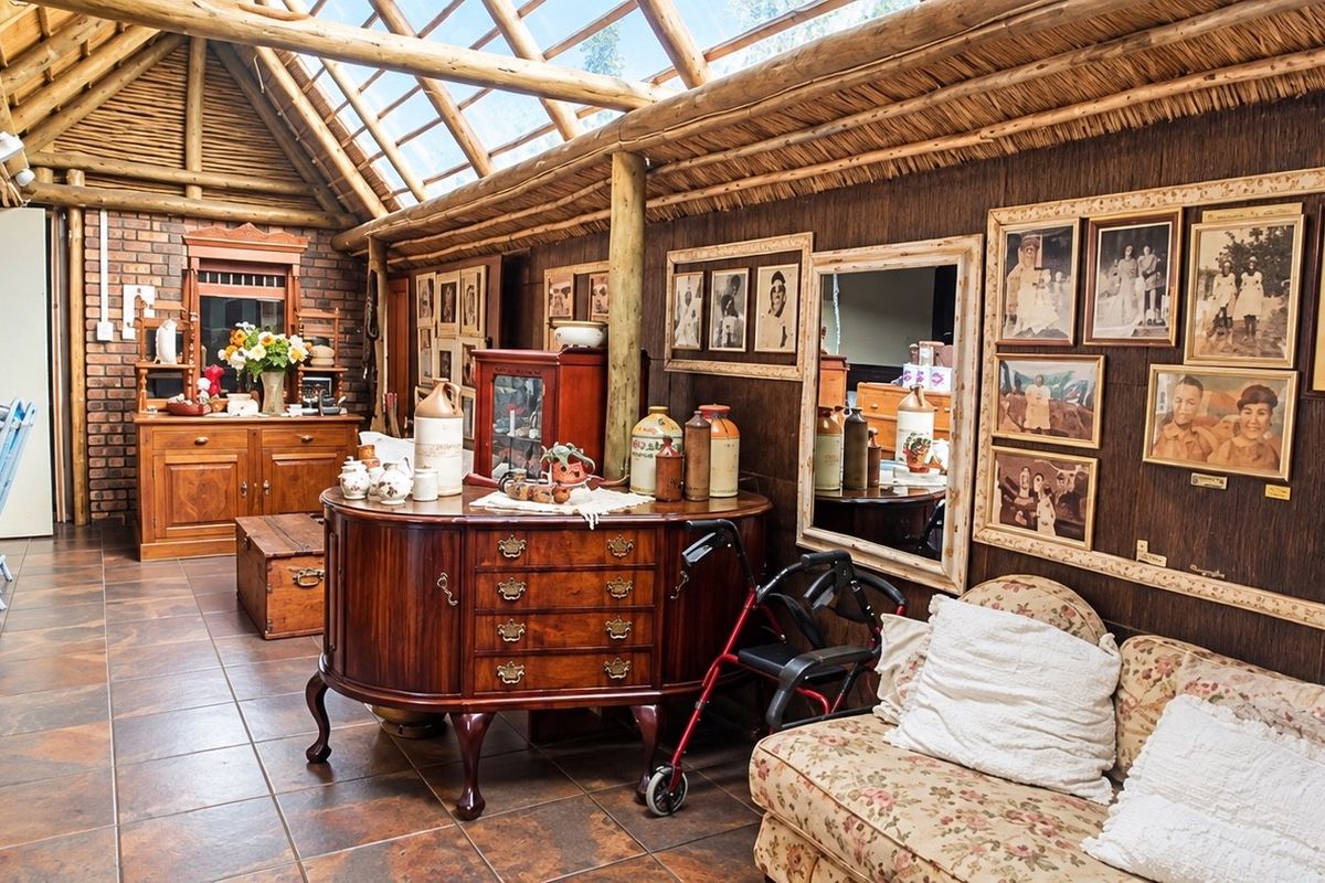 A rustic living area featuring exposed timber rafters, a thatched roof with integrated skylights, exposed brickwork, and durable tiled flooring.
