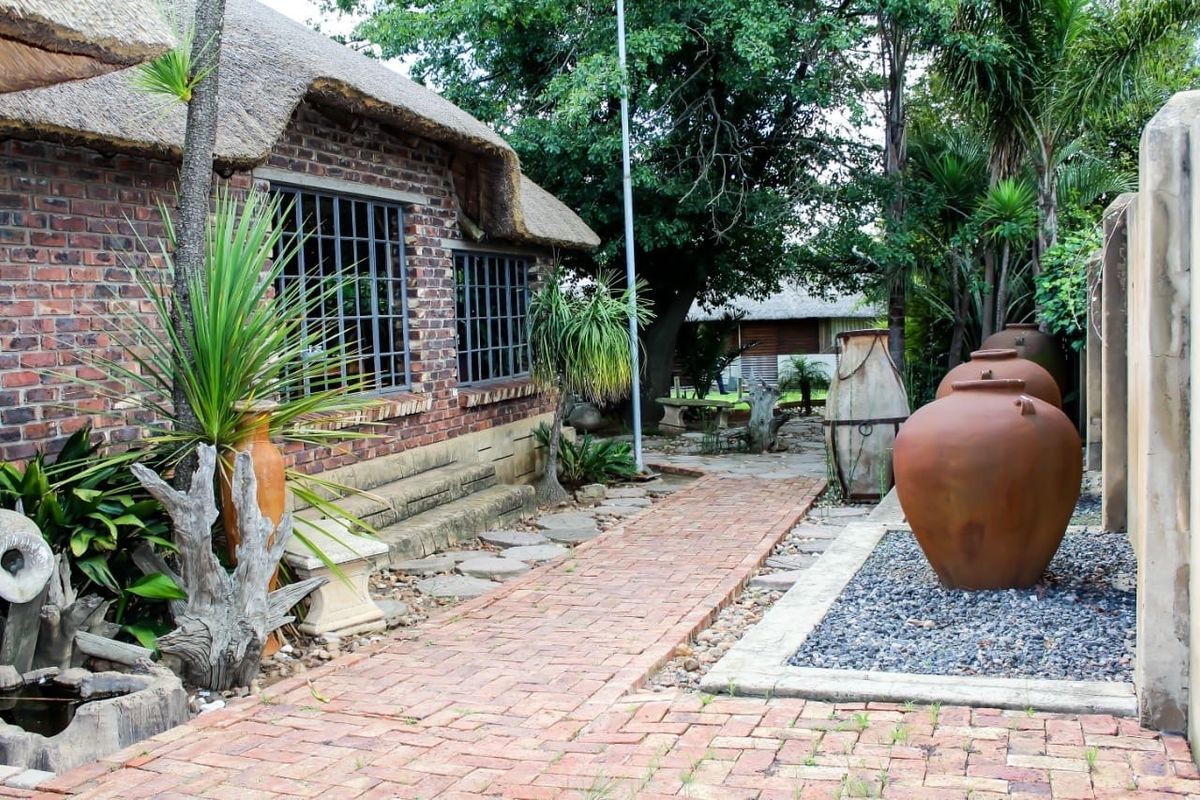 A charming rear garden area featuring a thatched roof building with exposed brickwork, a brick-paved walkway, and landscaped garden beds.
