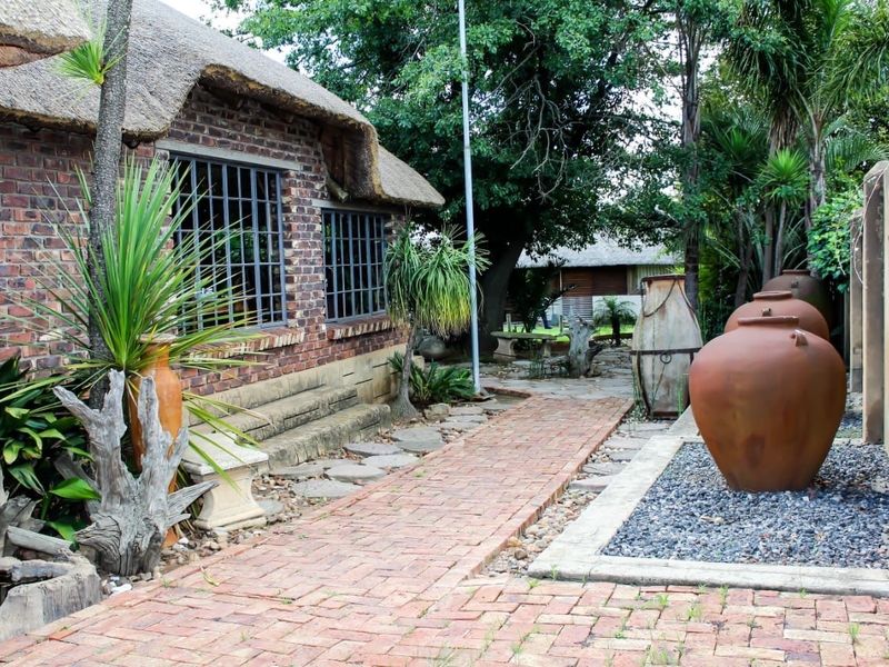 A charming rear garden area featuring a thatched roof building with exposed brickwork, a brick-paved walkway, and landscaped garden beds.