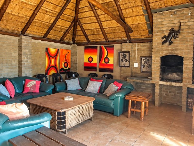 Spacious covered patio featuring a traditional thatched roof, exposed brick walls, and a built-in brick fireplace, ideal for outdoor entertaining.