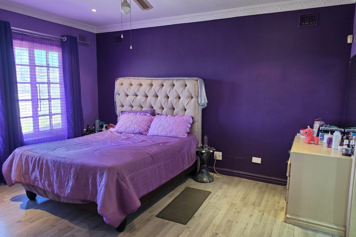 A bedroom featuring laminate flooring, crown molding, a ceiling fan, and french doors, currently finished with bold purple wall paint.