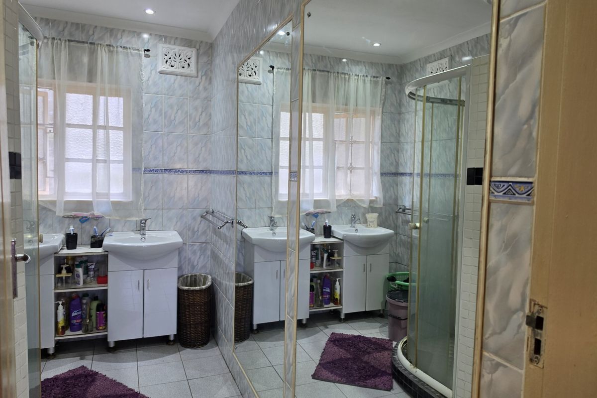 A functional bathroom featuring a double vanity, corner shower enclosure, and floor-to-ceiling wall tiling with a large mirror.
