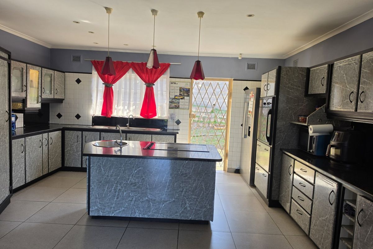 Spacious kitchen featuring a central island, built-in oven, hob, and extensive laminate cabinetry with tiled flooring and direct access to the rear exterior.