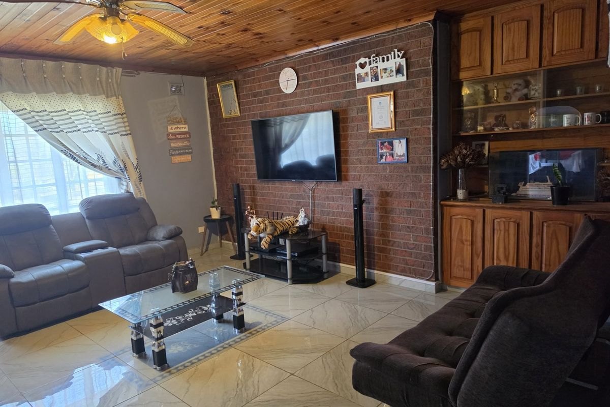 A living room featuring a distinctive timber ceiling, exposed brick feature wall, tiled flooring, and built-in wooden cabinetry for storage.