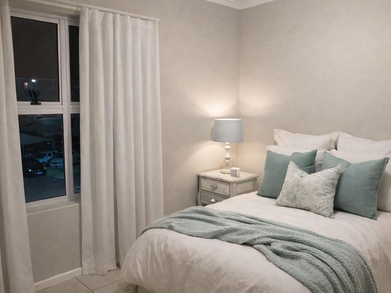 A well-maintained bedroom featuring neutral wall tones, tiled flooring, and a large window with modern curtains.