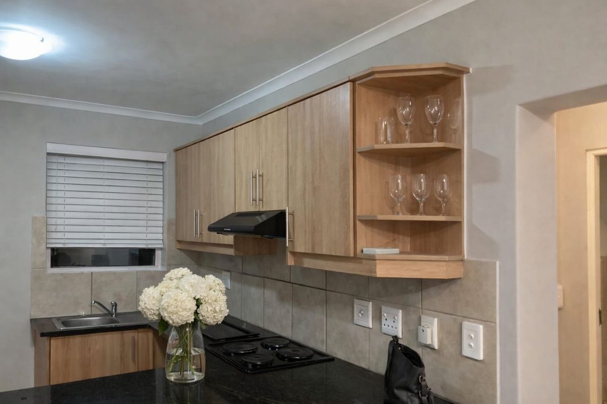 A well-maintained kitchen featuring light wood cabinetry, dark laminate countertops, a built-in electric hob with extractor fan, and a tiled backsplash.