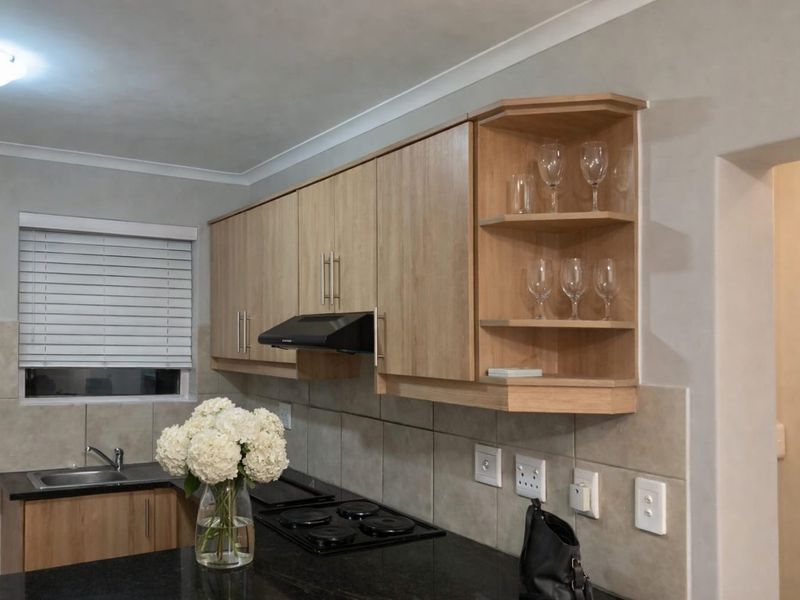 A well-maintained kitchen featuring light wood cabinetry, dark laminate countertops, a built-in electric hob with extractor fan, and a tiled backsplash.