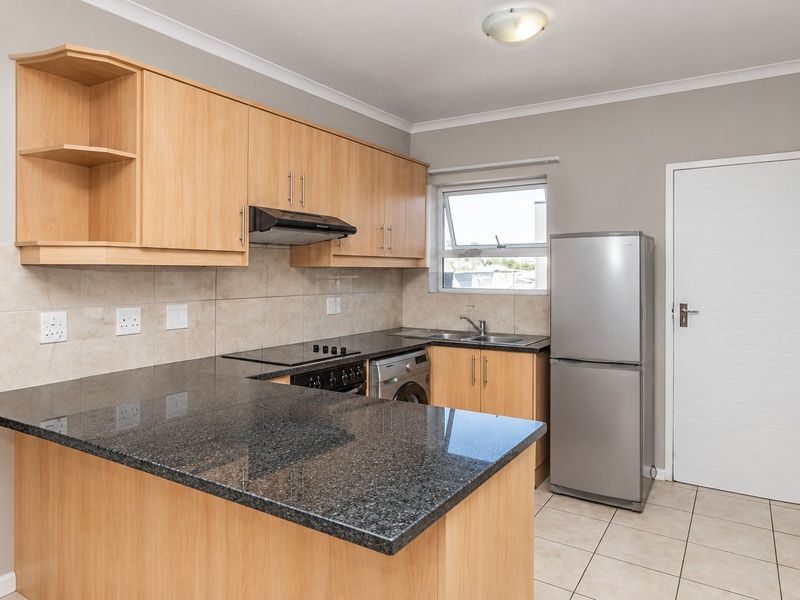A functional kitchen featuring granite countertops, light wood cabinetry, an electric hob with extractor, and tiled flooring, with an adjacent bathroom visible.