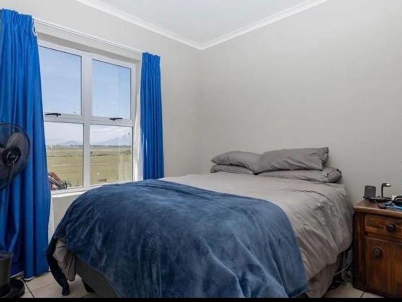 A functional bedroom featuring tiled flooring, neutral wall finishes, and an aluminium-framed window with views of the surrounding landscape.