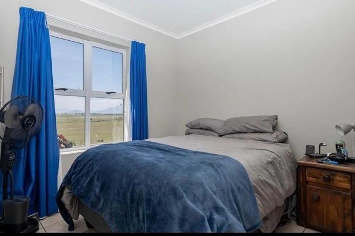 A functional bedroom featuring tiled flooring, neutral wall finishes, and an aluminium-framed window with views of the surrounding landscape.