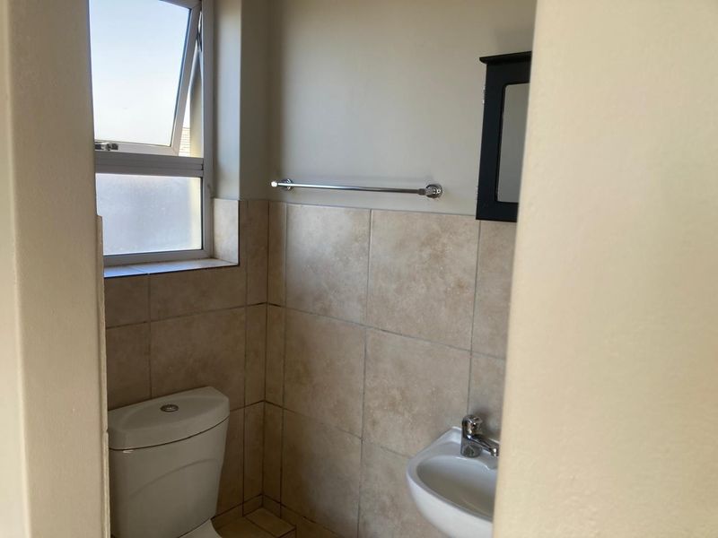 A compact bathroom featuring a toilet, wall-mounted basin, and tiled splashback, providing a functional and clean space.