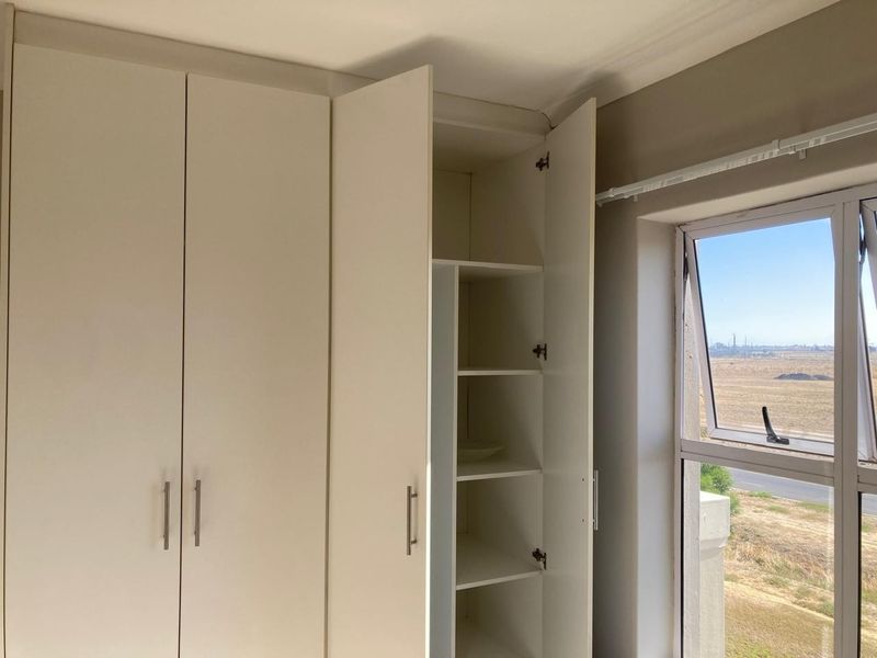 A bedroom featuring built-in cupboards with shelving and an aluminium window frame offering an exterior view.