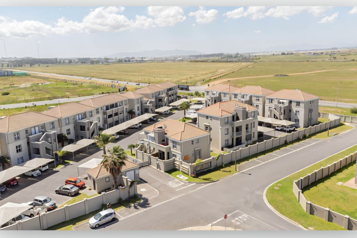 Aerial view of a modern apartment complex featuring multiple residential blocks, paved parking areas with carports, and secure perimeter fencing.