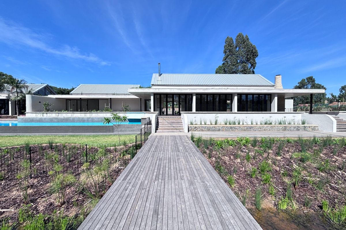 Rear exterior view of a modern townhouse featuring a timber walkway, swimming pool, and expansive patio area with bi-fold doors.
