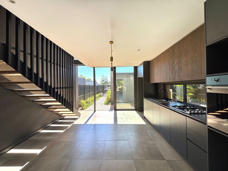 Modern open-plan kitchen and living area featuring sleek cabinetry, built-in appliances, tiled floors, and a striking staircase, opening onto a private rear garden.