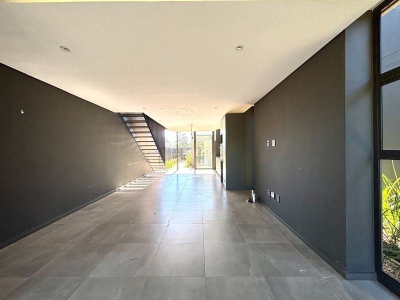 Spacious open-plan living area featuring modern dark-toned walls, large format floor tiles, recessed lighting, and a sleek staircase leading to the upper level.