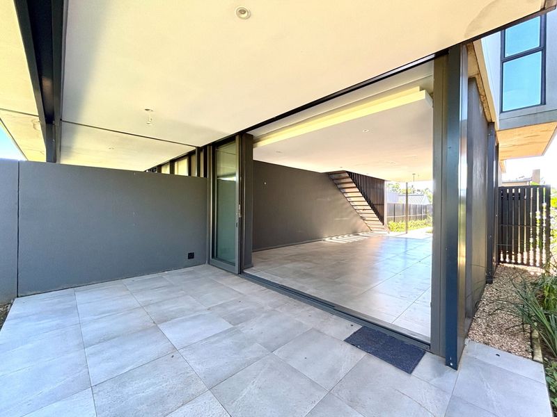 A modern, covered patio area featuring large format floor tiles, recessed lighting, and seamless indoor-outdoor flow through expansive sliding glass doors.