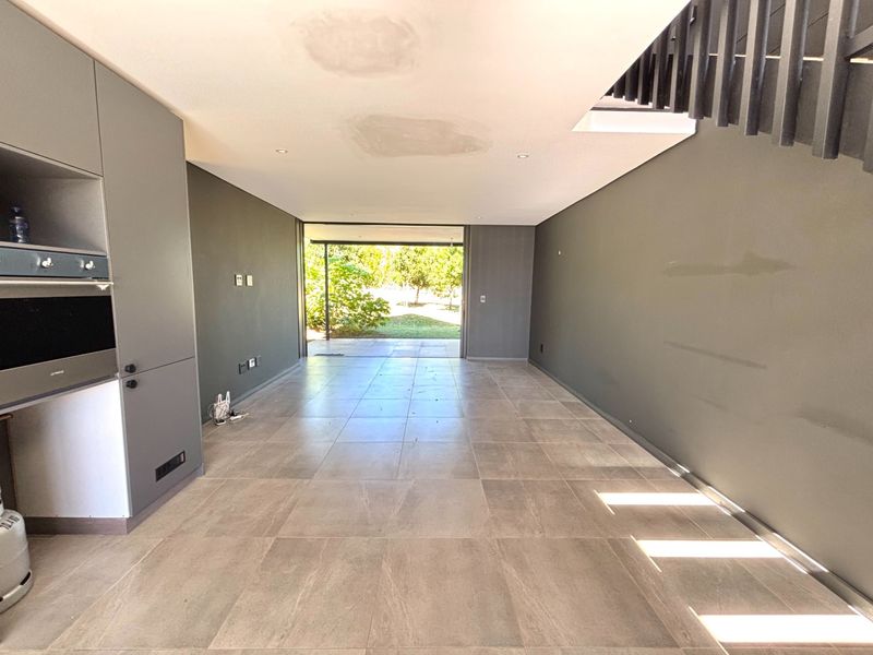 Spacious open-plan living area featuring large format floor tiles, built-in cabinetry with integrated oven, and direct access to the rear garden.