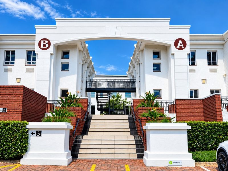 Front elevation of a commercial office complex featuring a central staircase, pedestrian bridge, and well-maintained brick and white facade.