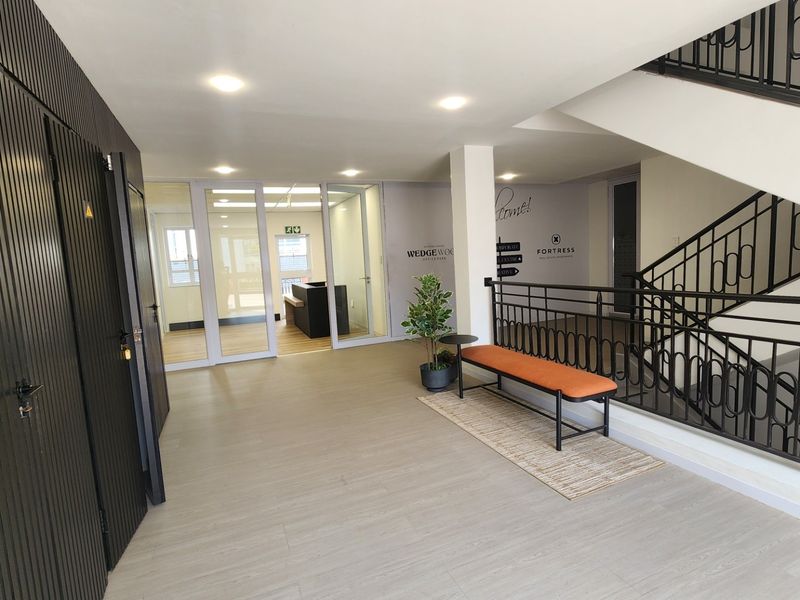 Modern commercial building entrance lobby featuring a staircase with wrought iron balustrade, glass partition walls, and clean laminate flooring.