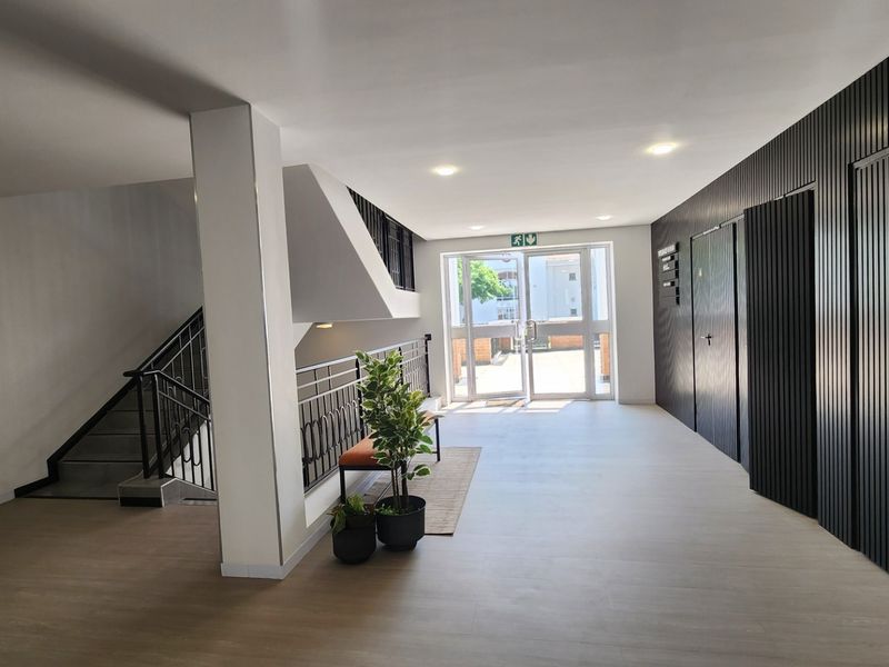 Modern commercial building entrance lobby featuring clean lines, slatted wall detailing, a staircase with metal balustrades, and a glass door leading to the exterior.