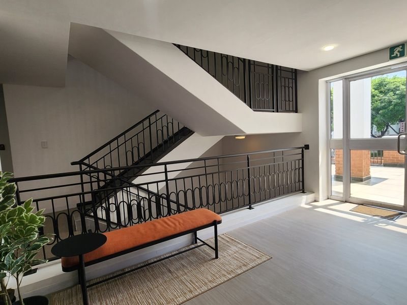 A bright, modern commercial hallway featuring a staircase with decorative metal balustrades and a glass door leading to an outdoor area.