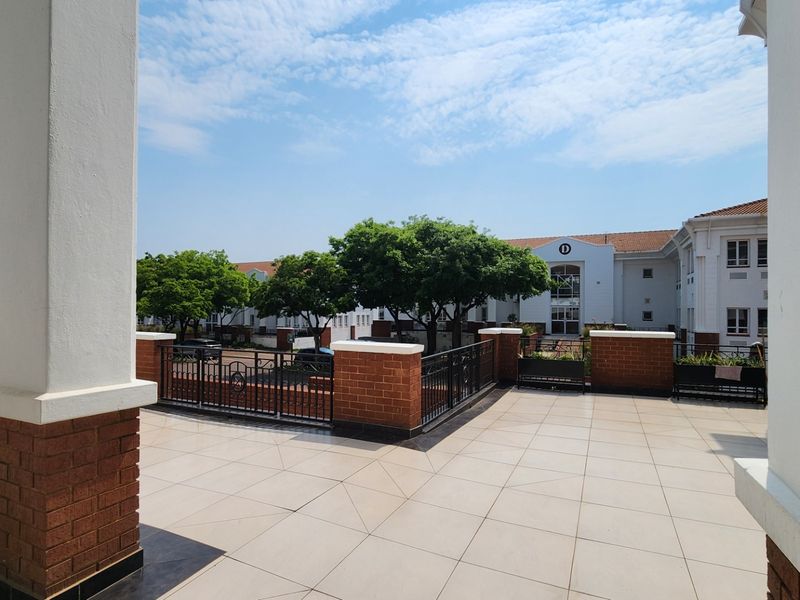 A spacious, well-maintained tiled balcony featuring brick pillars and wrought iron railings, overlooking the commercial property grounds.