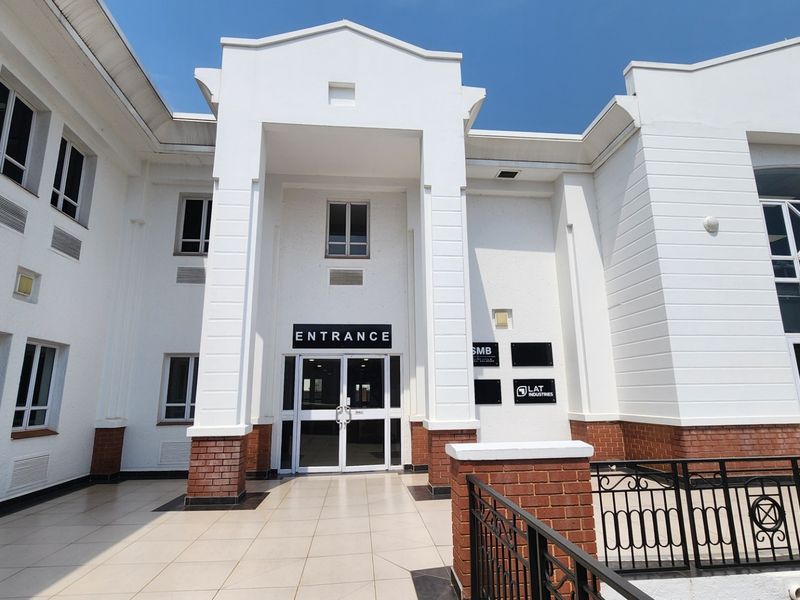 Commercial building entrance featuring a tiled patio, brick base detailing, and a prominent central doorway with glass panels.