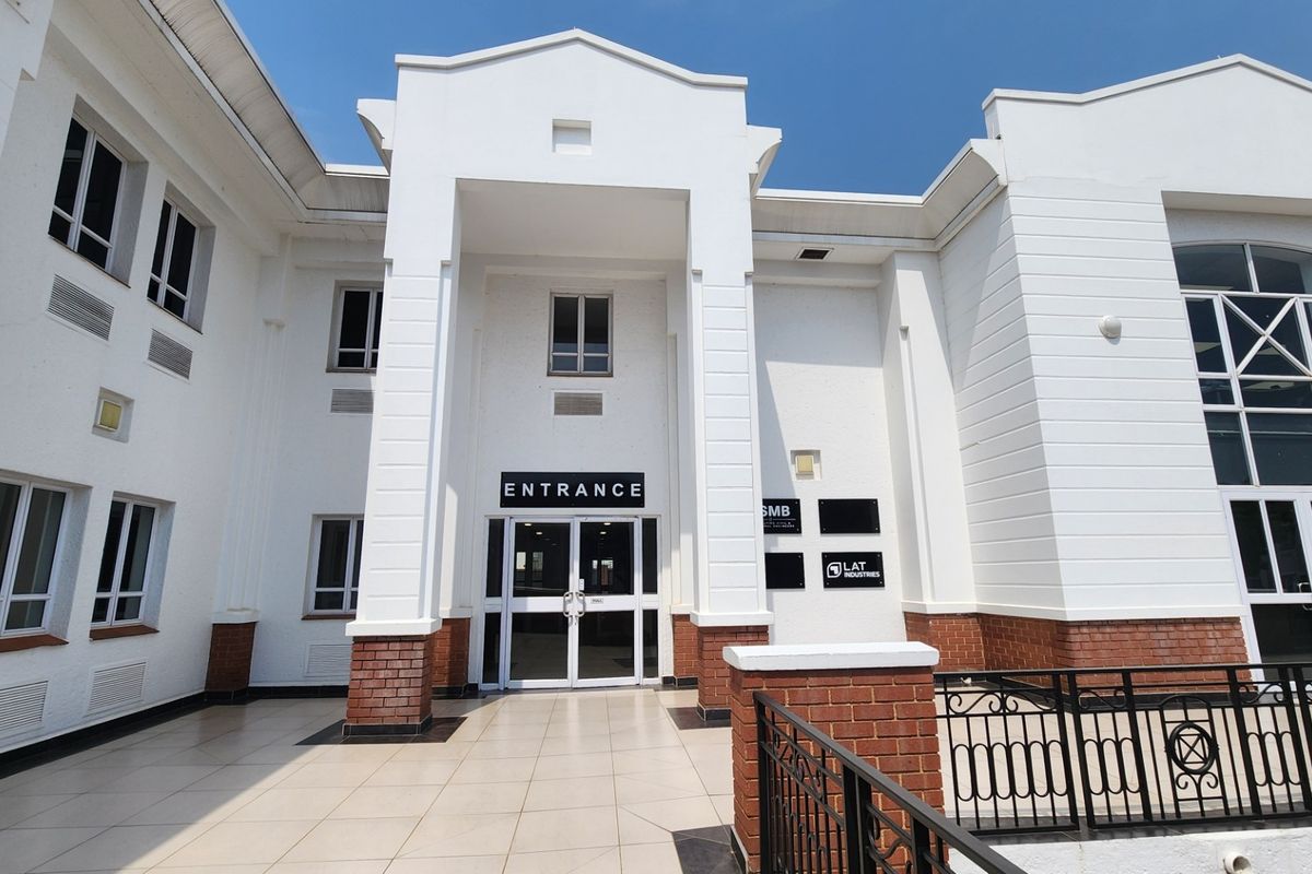 Commercial building entrance featuring a tiled patio, brick base detailing, and a prominent central doorway with glass panels.