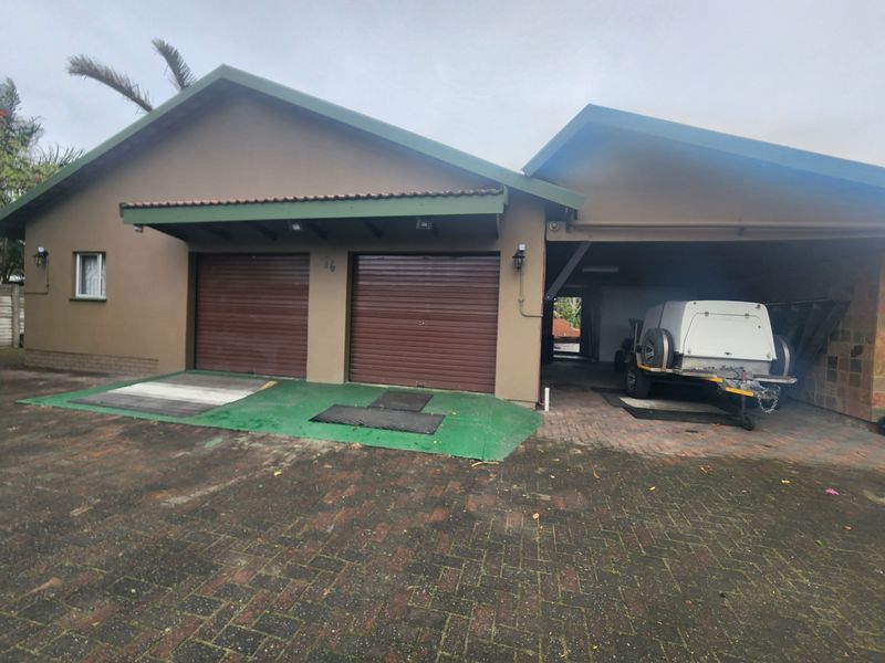 Exterior view of a double garage with roller doors and an adjacent covered carport area, featuring a paved driveway.