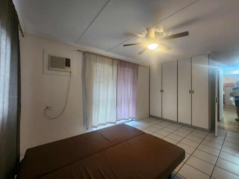 A bedroom featuring tiled flooring, built-in cupboards, a ceiling fan, and a window-mounted air conditioning unit.