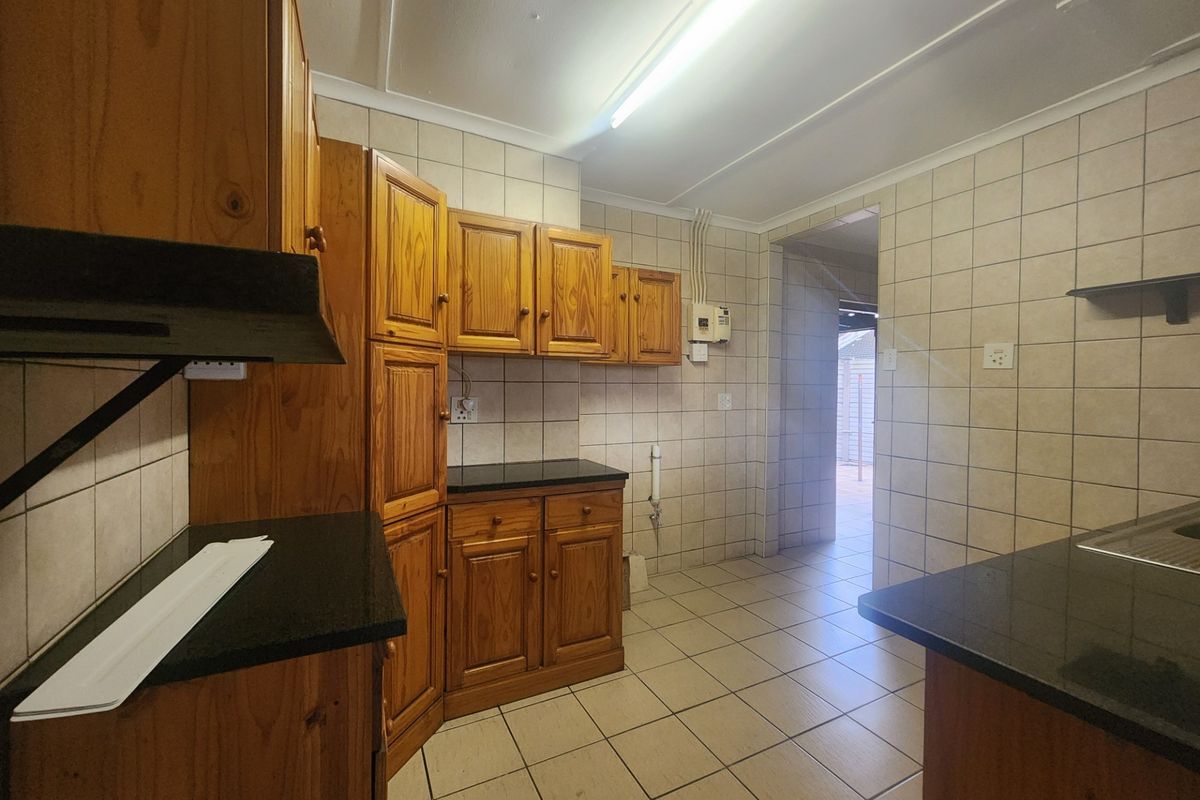 A functional kitchen featuring wooden cabinetry, granite countertops, and tiled finishes throughout, offering a clean and practical layout.