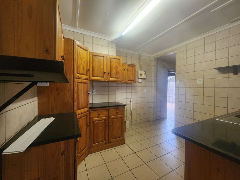 A functional kitchen featuring wooden cabinetry, granite countertops, and tiled finishes throughout, offering a clean and practical layout.