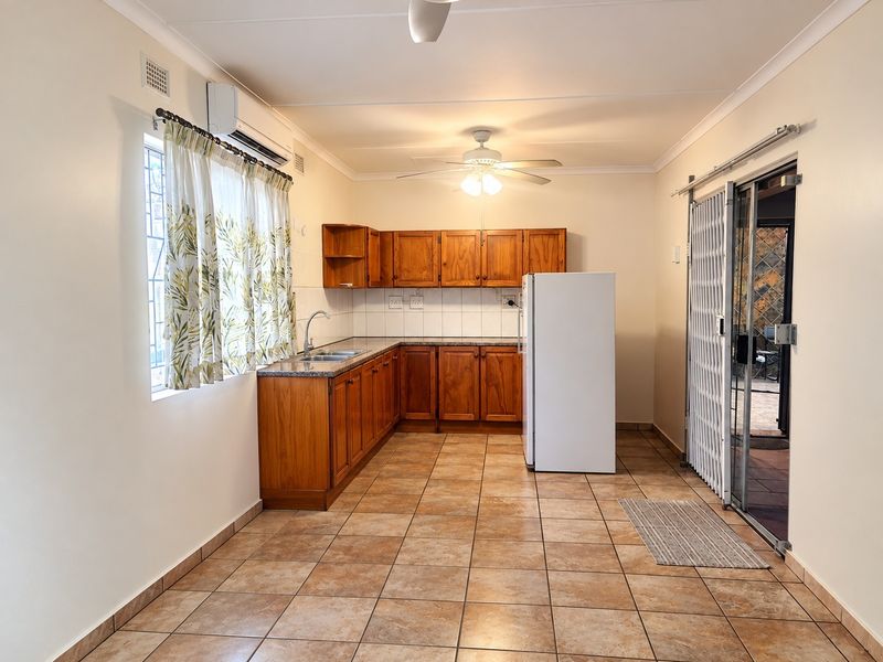 Functional kitchen featuring wooden cabinetry, granite countertops, tiled flooring, and direct access to an outdoor area through a security gate.