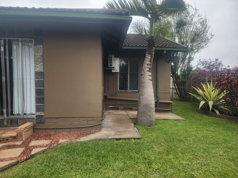 A view of the rear exterior of the house featuring a concrete pathway, landscaped garden, and mounted air conditioning unit.